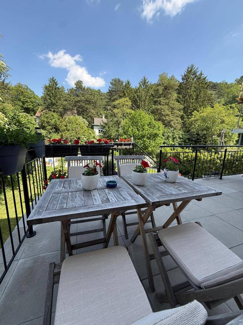 Geräumiger Balkon mit zwei Holztischen und weitem Blick auf die grüne Umgebung.