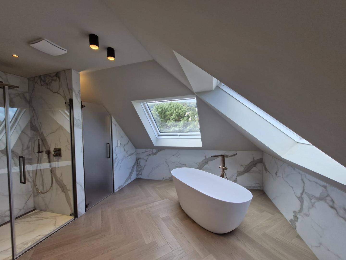Luxuriöses Badezimmer im Dachgeschoss mit freistehender Badewanne, Dusche und Marmorwänden.