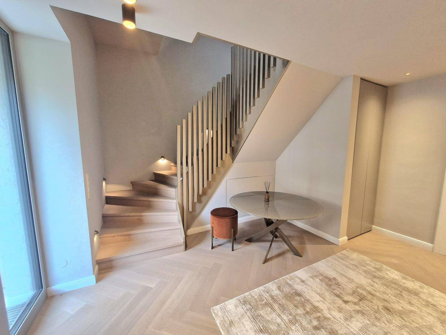 Elegantes Treppenhaus mit Holzstufen, modernem Geländer und Fischgrätparkett in hellem Ambiente.