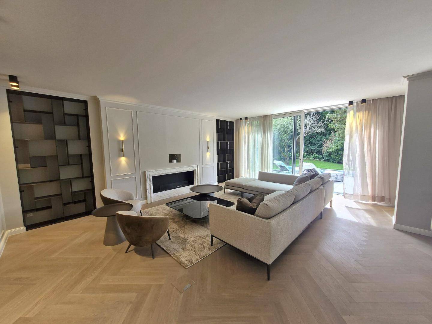 Gemütliches Wohnzimmer mit modernem Kamin, bequemen Sofas und Blick auf den Garten mit Pool.