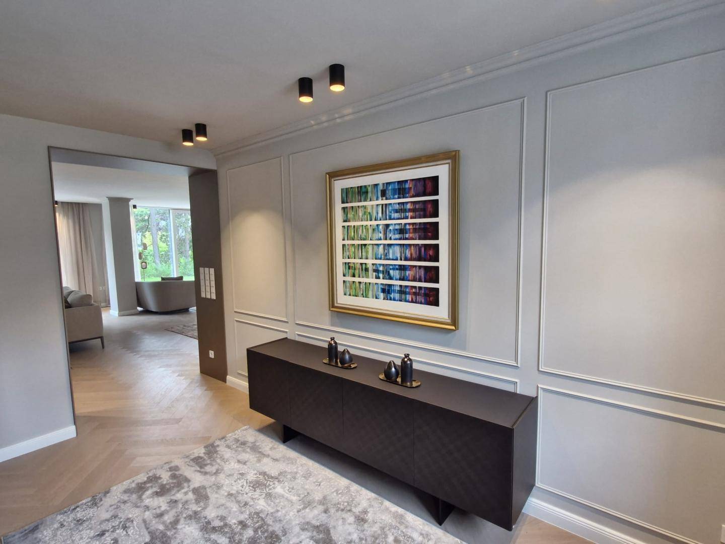 Eleganter Flurbereich mit Wandvertäfelung, modernem Sideboard und Kunstwerk, offen zum Wohnbereich.