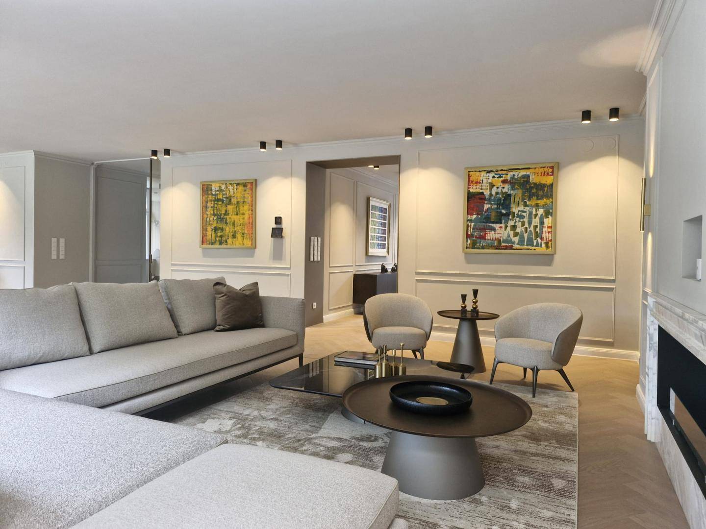 Moderner Wohnbereich mit bequemen Sofas, Kunstwerken und Fischgrätparkett, offen zum Esszimmer.
