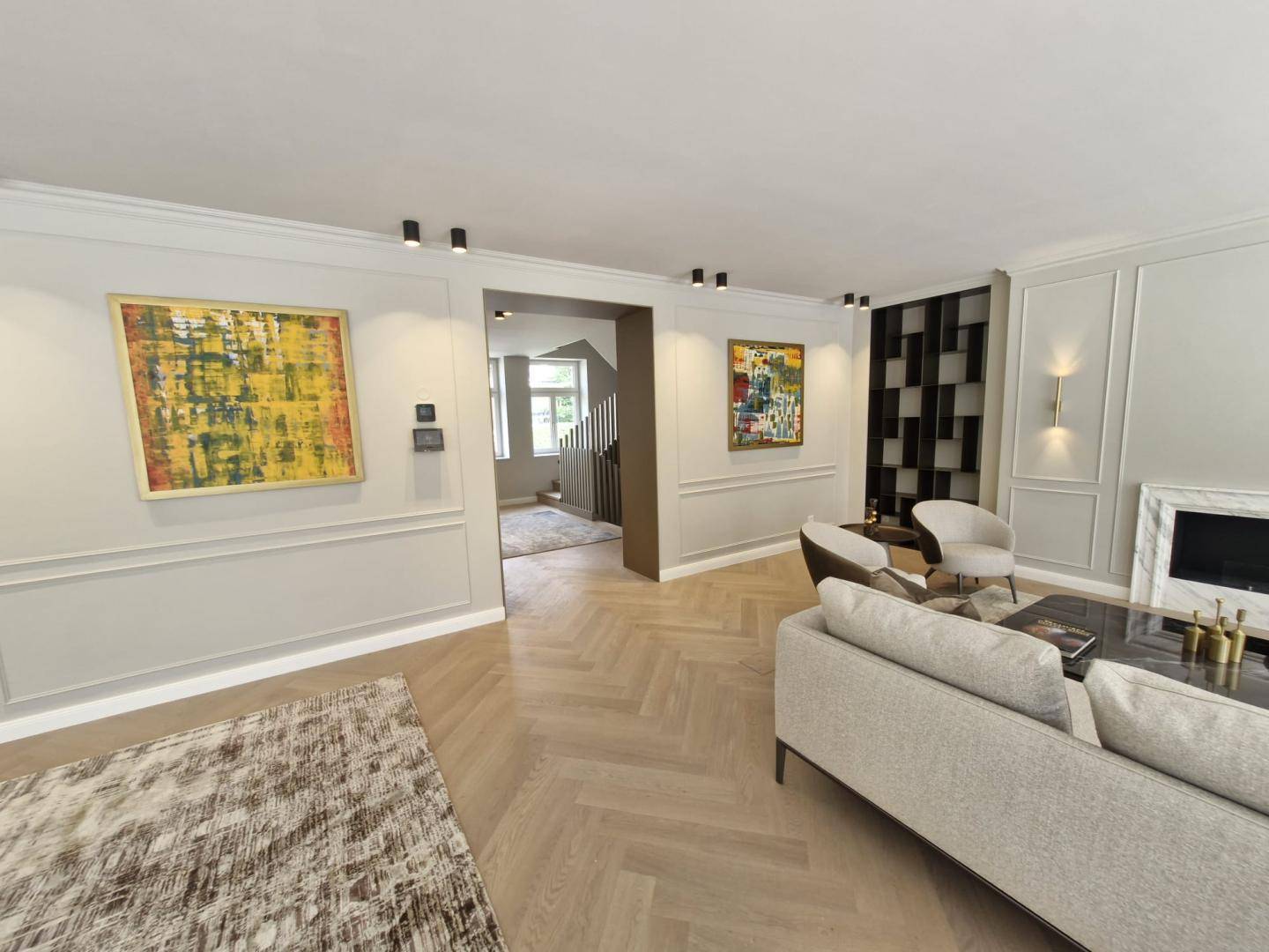 Helles Wohnzimmer mit modernem Kamin, bequemen Sofas und Fischgrätparkett, offen zum Treppenhaus.