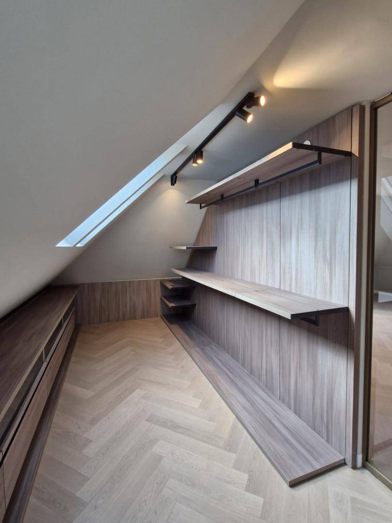Geräumiger begehbarer Kleiderschrank im Dachgeschoss mit Holzregalen und Fischgrätparkett.