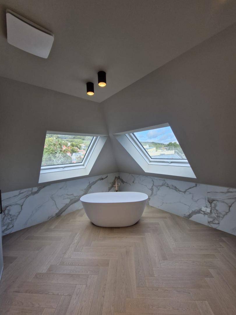 Elegantes Badezimmer im Dachgeschoss mit freistehender Badewanne, Marmorwänden und zwei Dachfenstern.