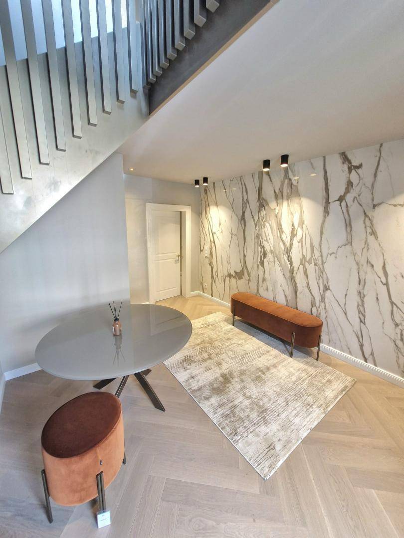 Moderner Eingangsbereich mit Marmorwand, Fischgrätparkett und stilvoller Treppe zum Obergeschoss.