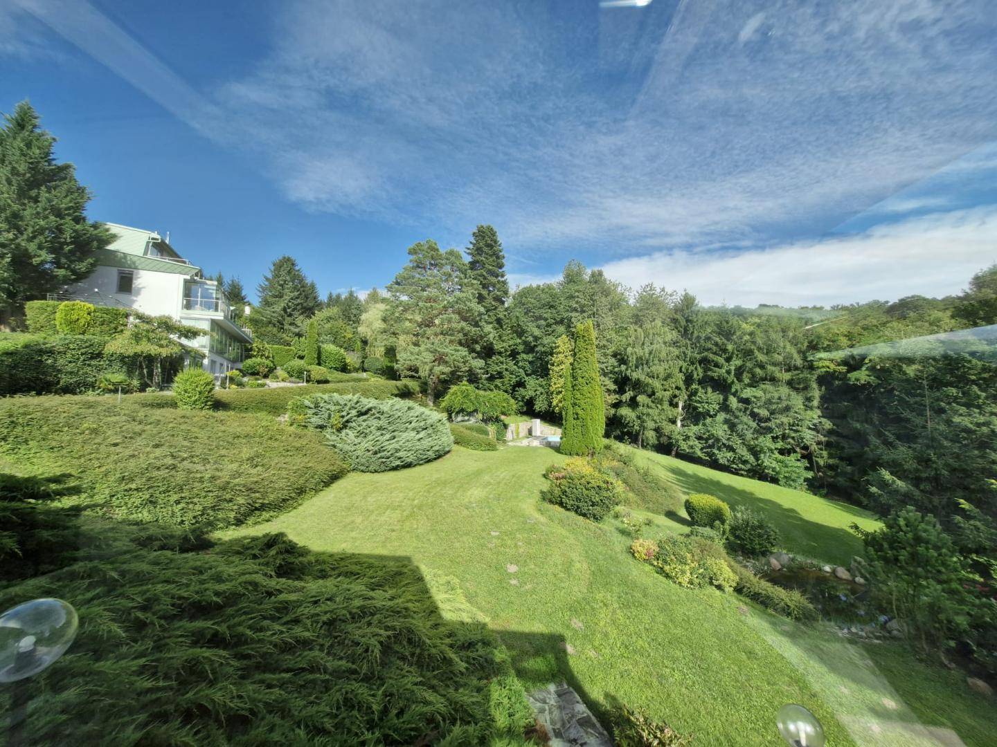 Weitläufiger, gepflegter Garten mit üppiger Vegetation und einem Teil des Hauses im Hintergrund.