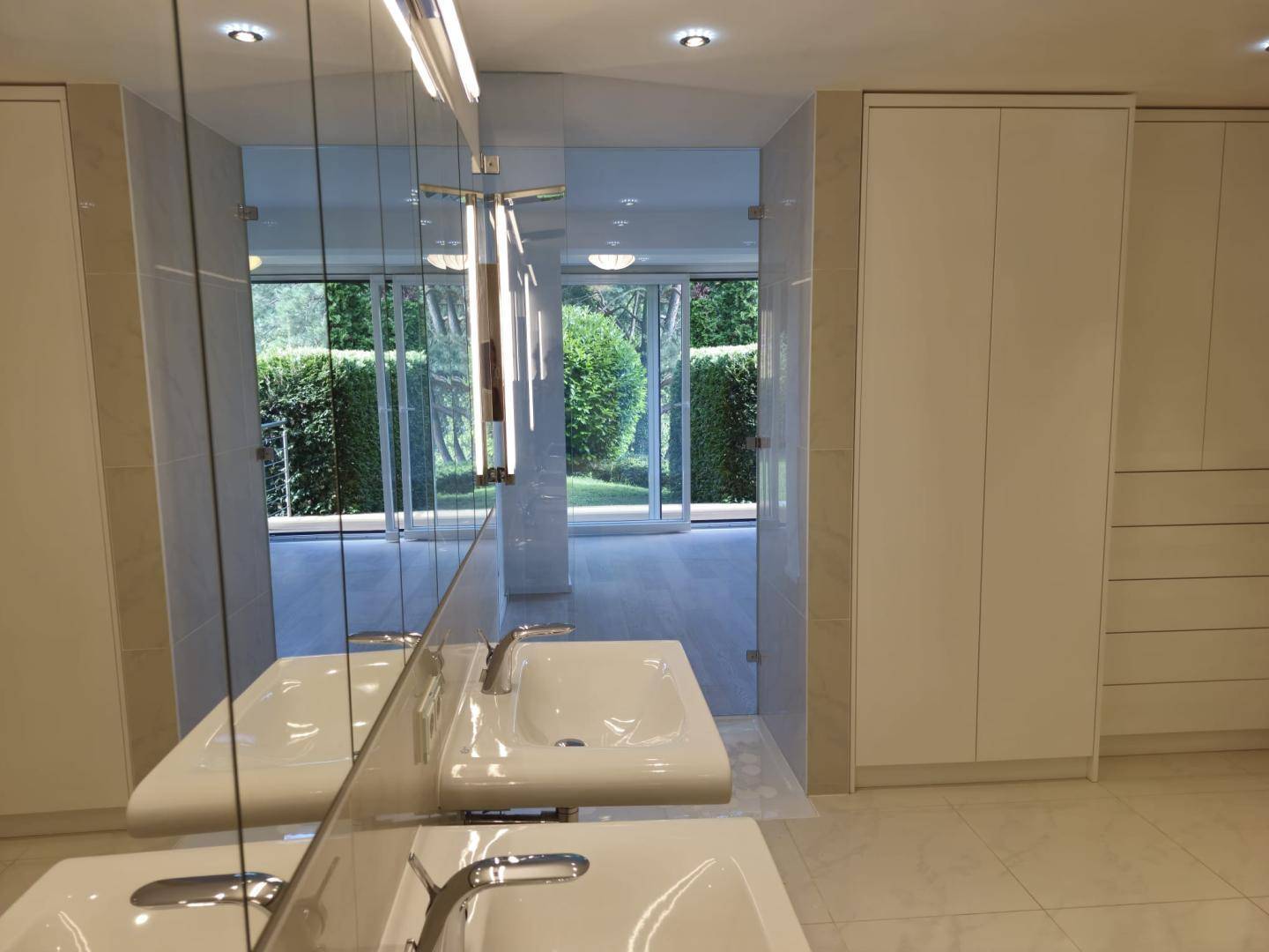 Helles Badezimmer mit Doppelwaschbecken und Spiegelschrank, der den Blick ins Grüne reflektiert.