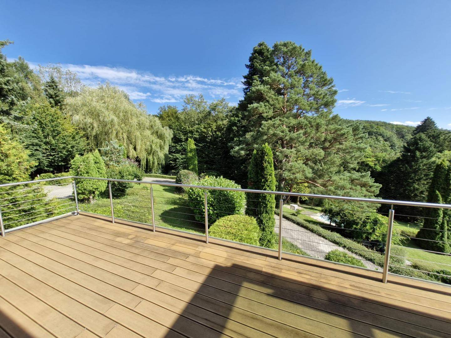 Geräumiger Holzdeck-Balkon mit modernem Geländer und weitem Blick auf den grünen Garten.