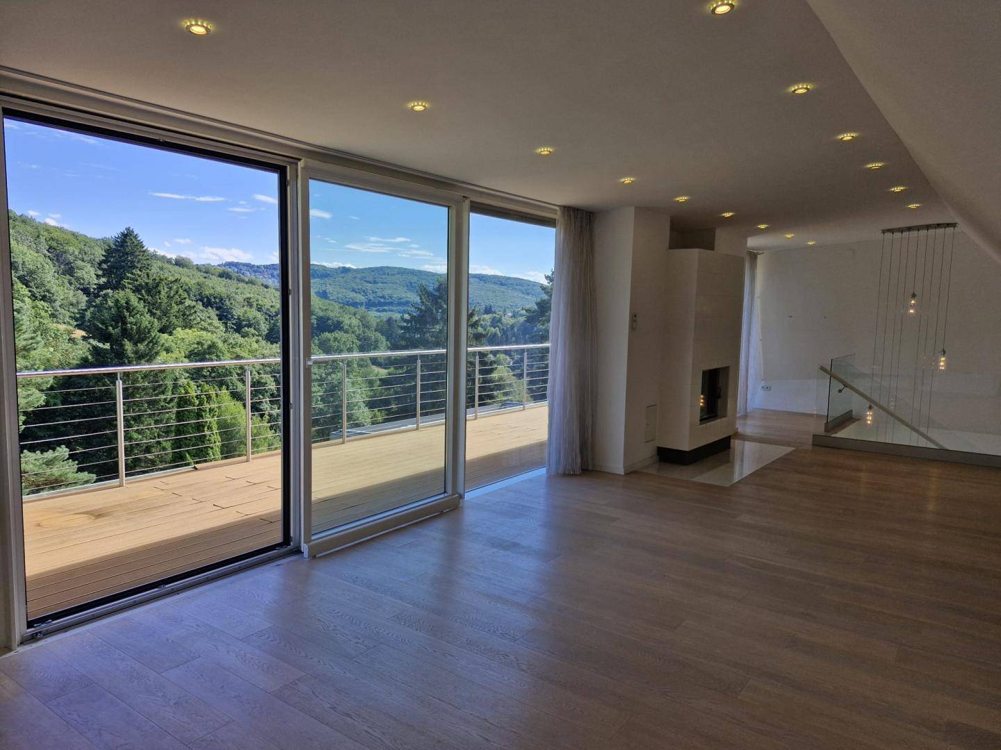 Helles Wohnzimmer mit Holzboden, modernem Kamin und Zugang zu einem Balkon mit Panoramablick.