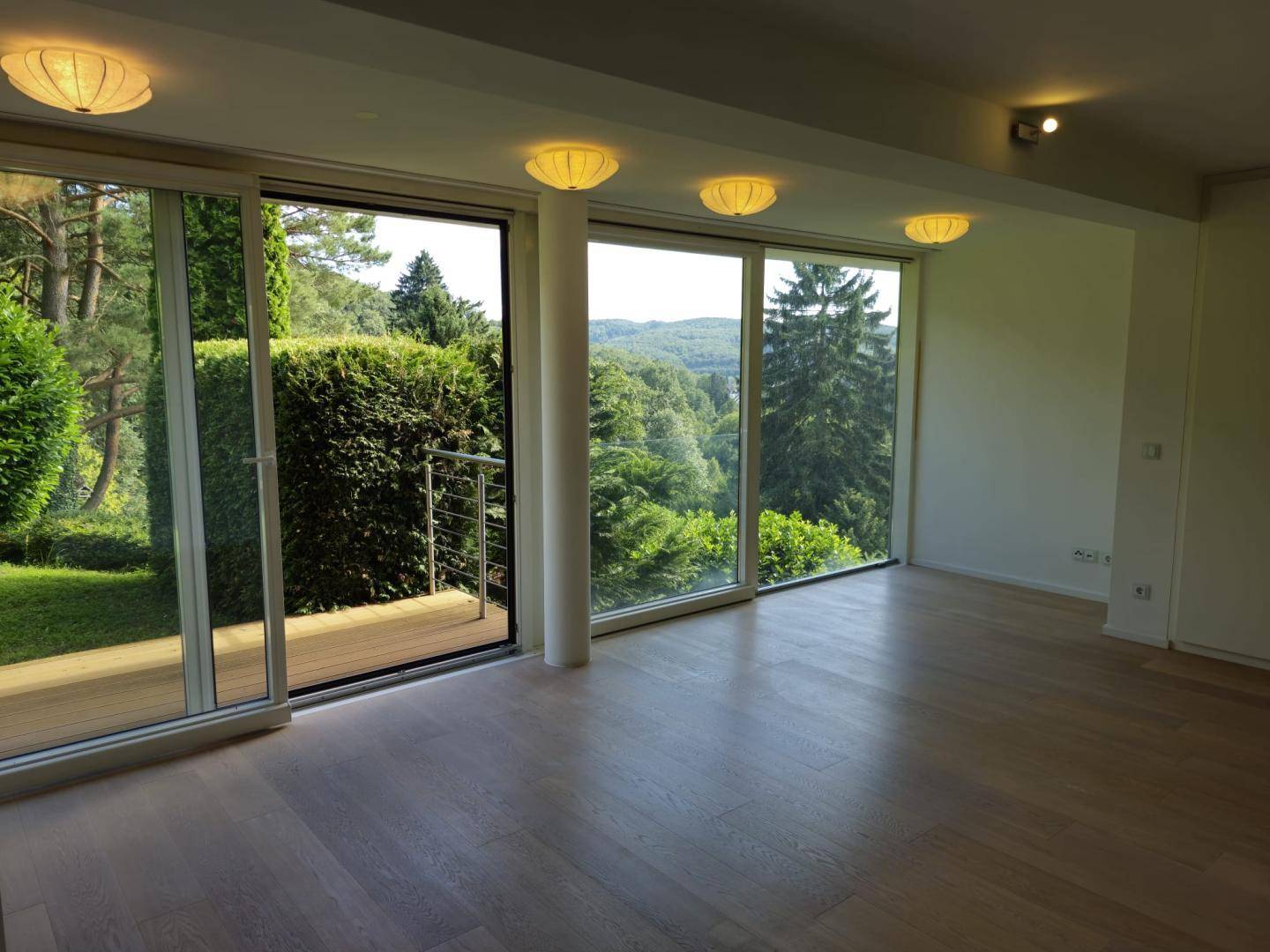 Geräumiger Wohnbereich mit Holzboden und raumhohen Fenstern, die einen weiten Blick ins Grüne ermöglichen.