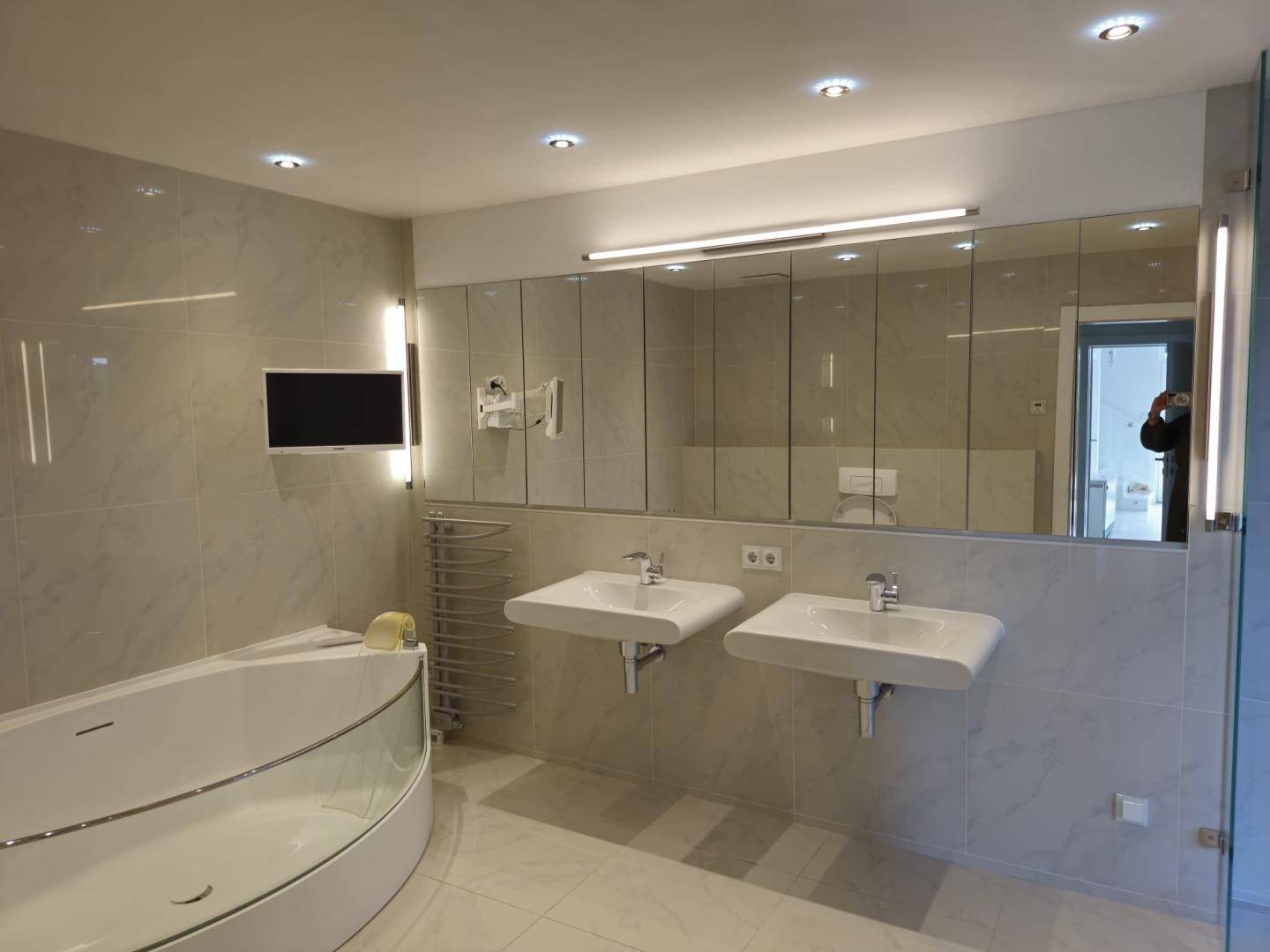 Modernes Badezimmer mit großer Eckbadewanne, Doppelwaschbecken und integriertem Fernseher.