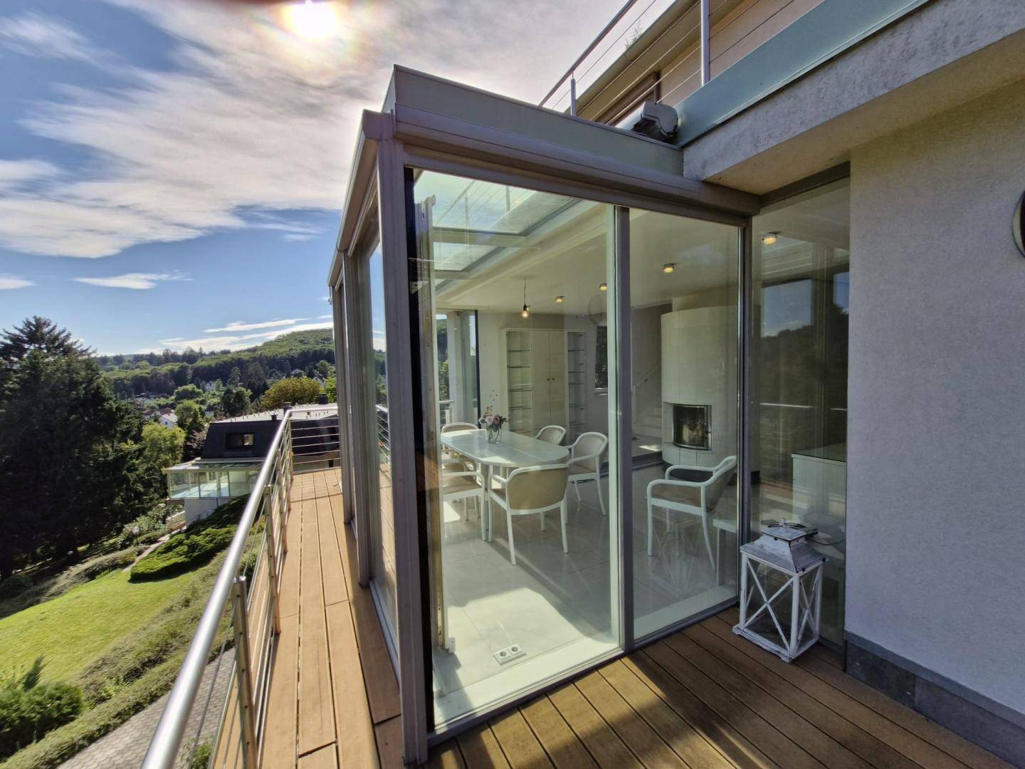 Verglaster Essbereich im Freien mit Tisch und Stühlen, angrenzend an ein Holzdeck mit Weitblick.