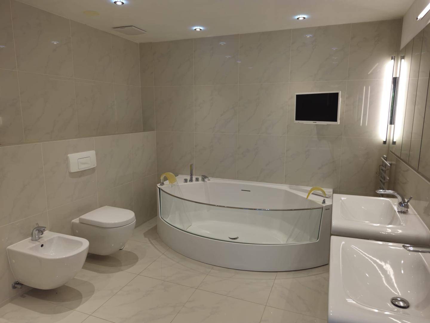 Elegantes Badezimmer mit Eckbadewanne, wandhängendem WC, Bidet und zwei Waschbecken.