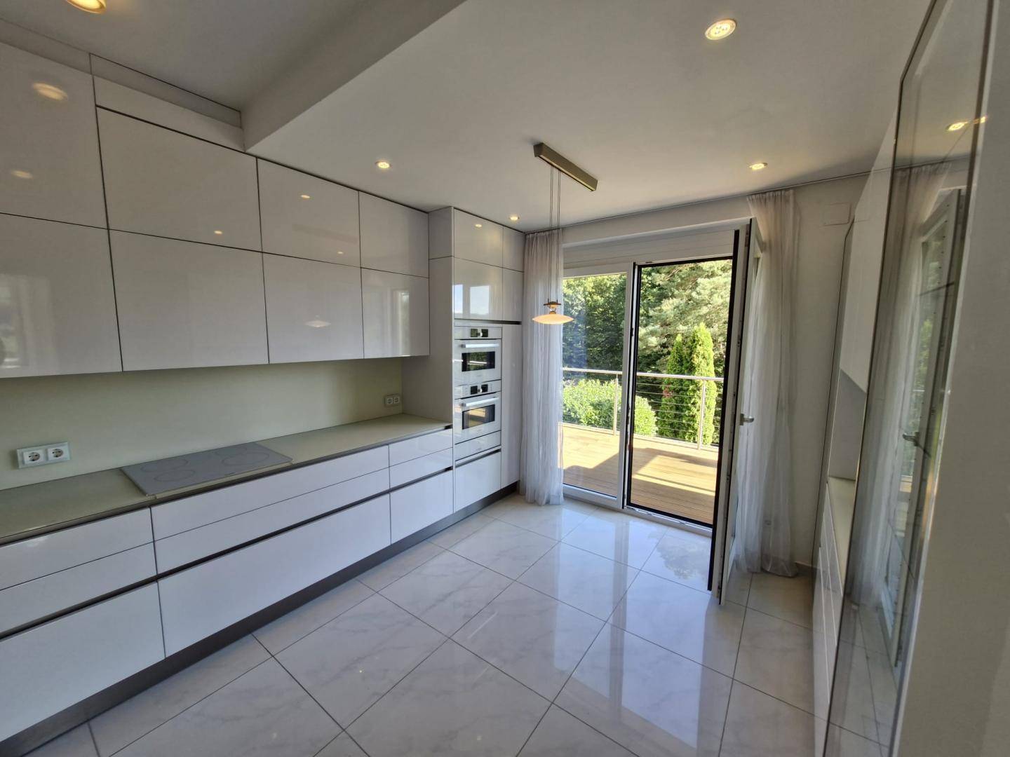 Moderne Küche mit weißen Hochglanzfronten, Einbaugeräten und Zugang zu einem Balkon.