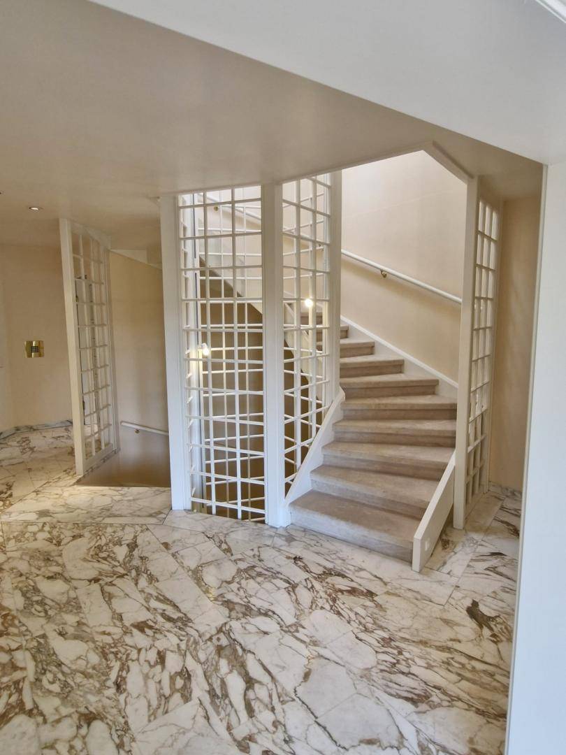 Elegantes Treppenhaus mit kunstvollem Gittergeländer und glänzendem Marmorboden im Eingangsbereich.
