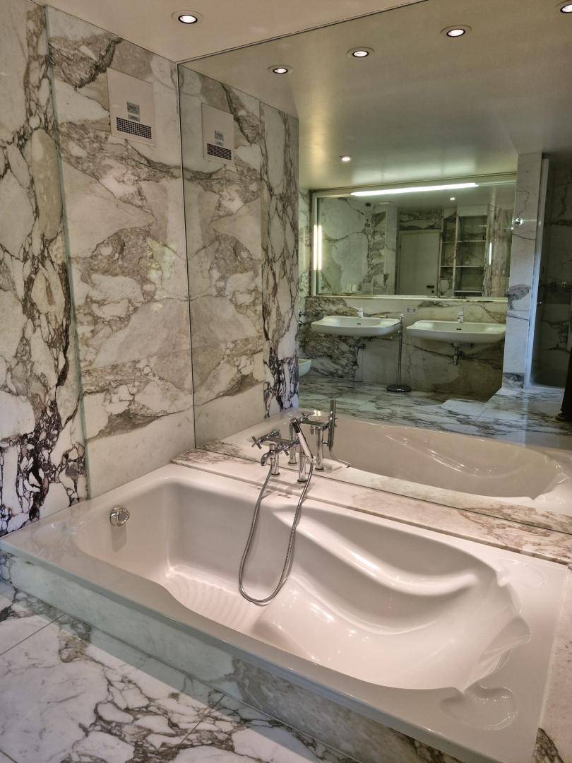 Großzügiges Badezimmer mit eingebauter Badewanne, umgeben von edlem Marmor und großen Spiegeln.
