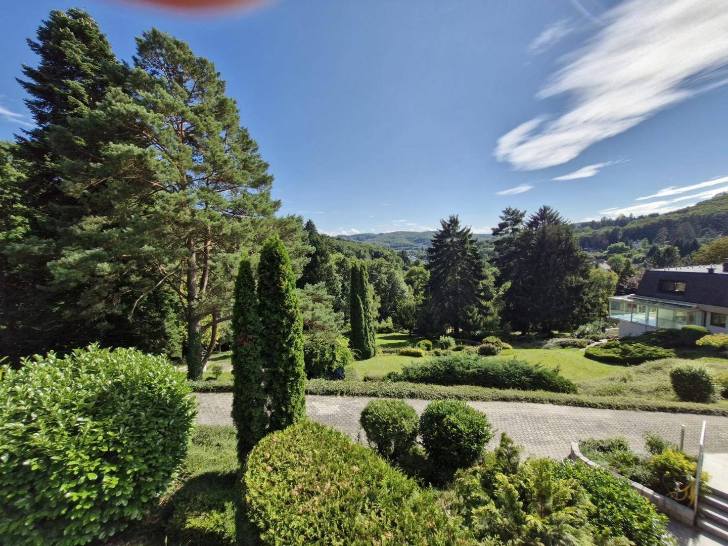 Weitläufiger Garten mit hohen Bäumen, gepflegten Büschen und einer malerischen Hügellandschaft.