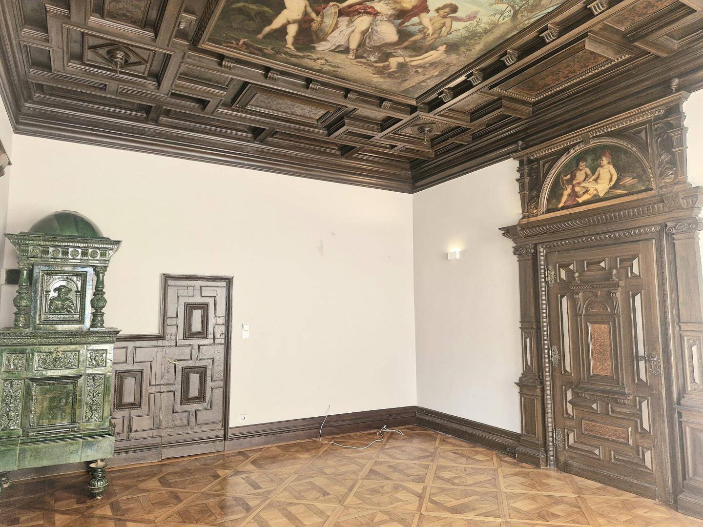 Historischer Raum mit aufwendiger Kassettendecke, Kachelofen und Fischgrätparkett.