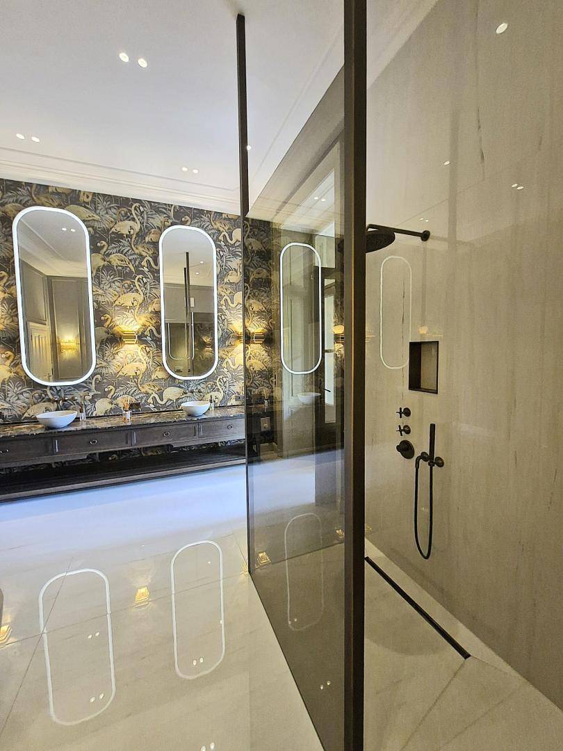 Modernes Badezimmer mit begehbarer Dusche, doppelten Waschbecken und gemusterter Tapete.