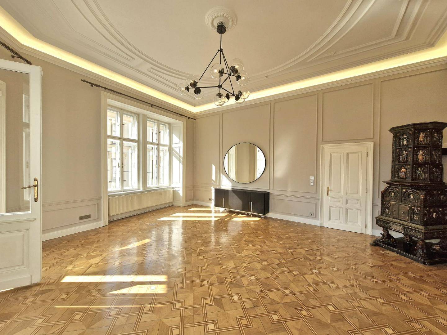 Geräumiges Wohnzimmer mit Fischgrätparkett, Stuckdecke und traditionellem Kachelofen.