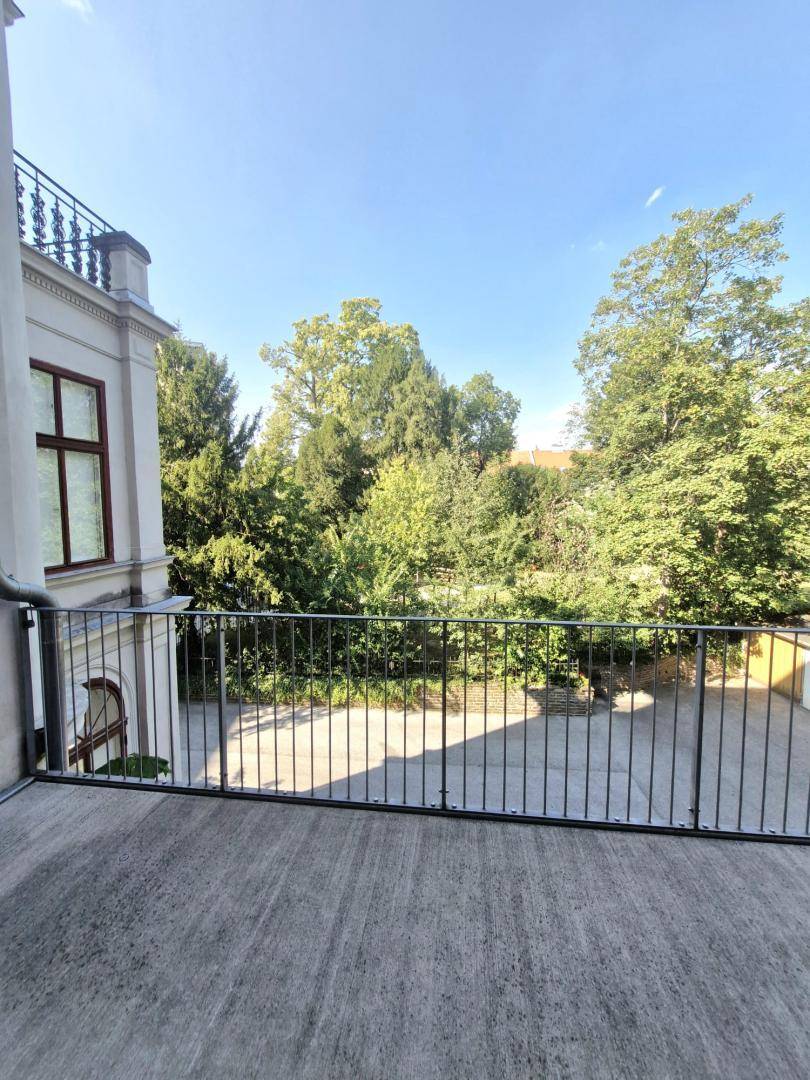 Balkon mit Blick auf einen grünen Innenhof und alte Bäume.