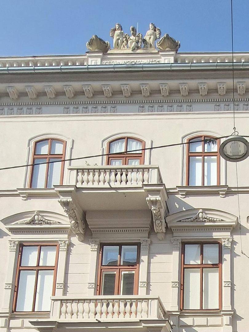 Historische Fassade mit verzierten Balkonen und Skulpturen auf dem Dach.