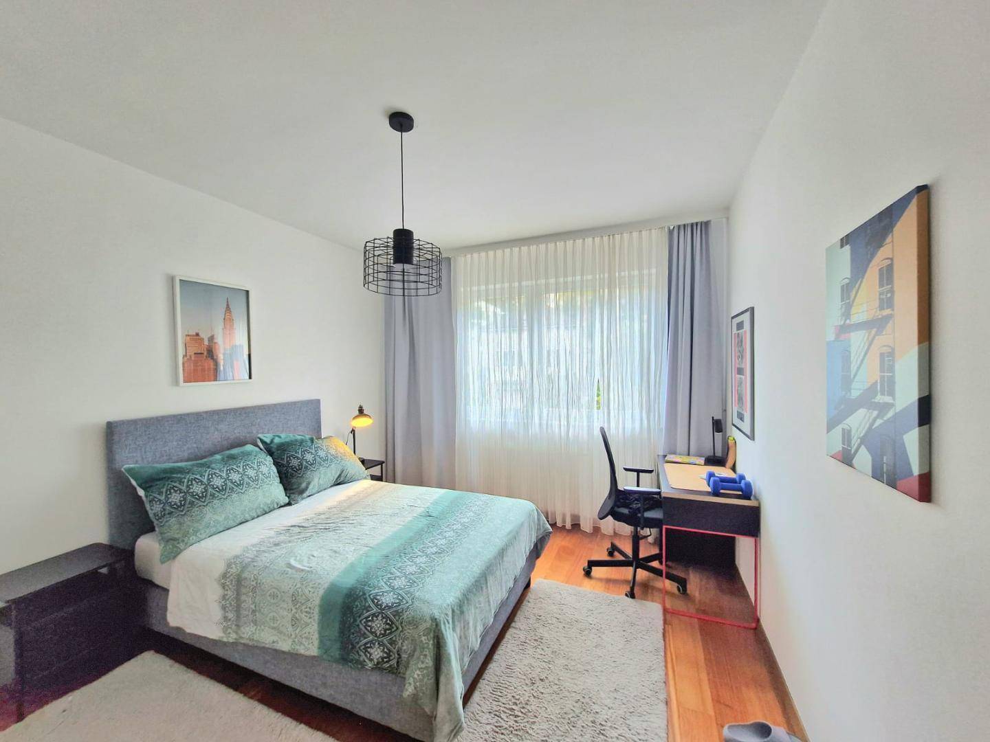 Modernes Schlafzimmer mit Doppelbett, Schreibtisch und großem Fenster für viel Tageslicht.