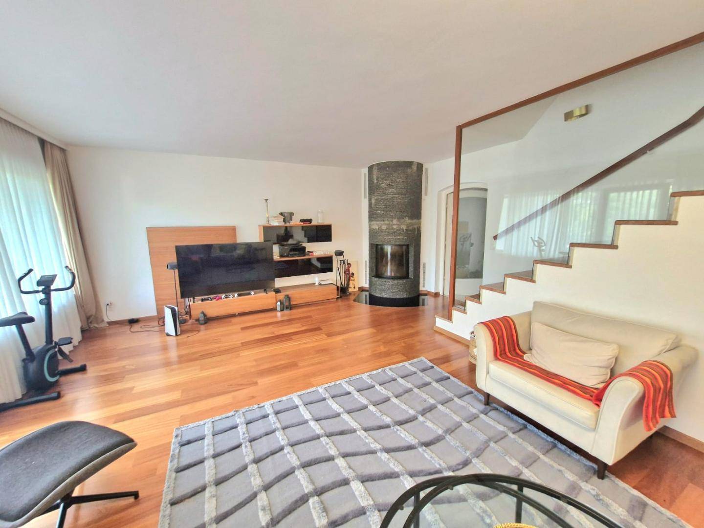 Geräumiges Wohnzimmer mit modernem Kamin, Holzboden und Fitnessbereich neben der Treppe.