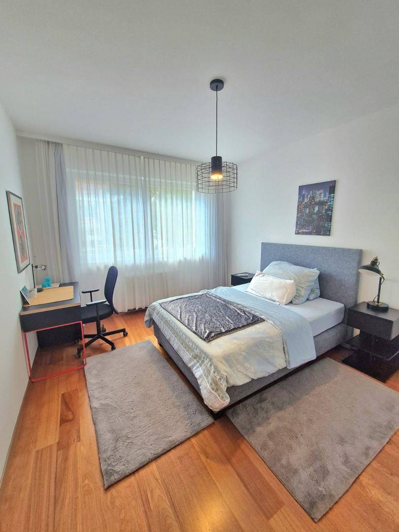 Helles Schlafzimmer mit Holzboden, Schreibtisch und großem Fenster, ideal für Arbeit und Erholung.