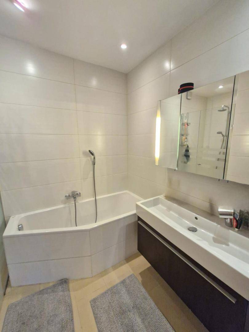 Modernes Badezimmer mit Badewanne, Waschtisch und Spiegelschrank, hell gefliest und funktional.