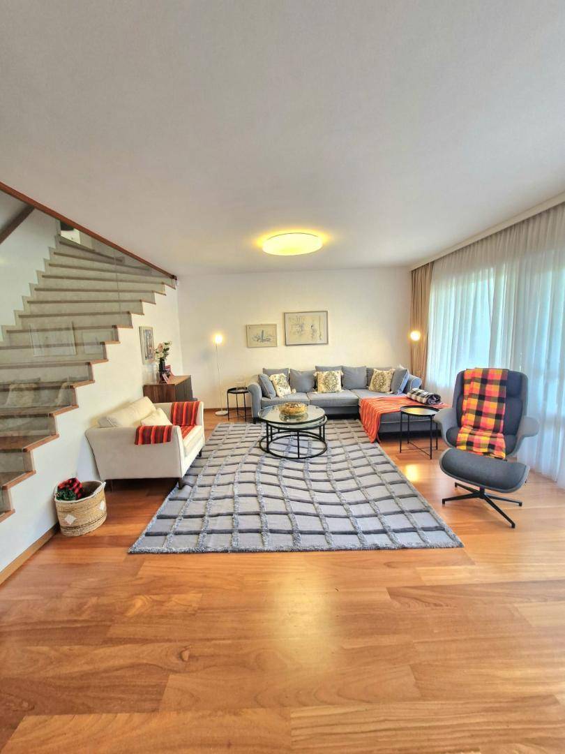 Großzügiges Wohnzimmer mit bequemer Sofalandschaft, Holzboden und moderner Treppe mit Glasgeländer.