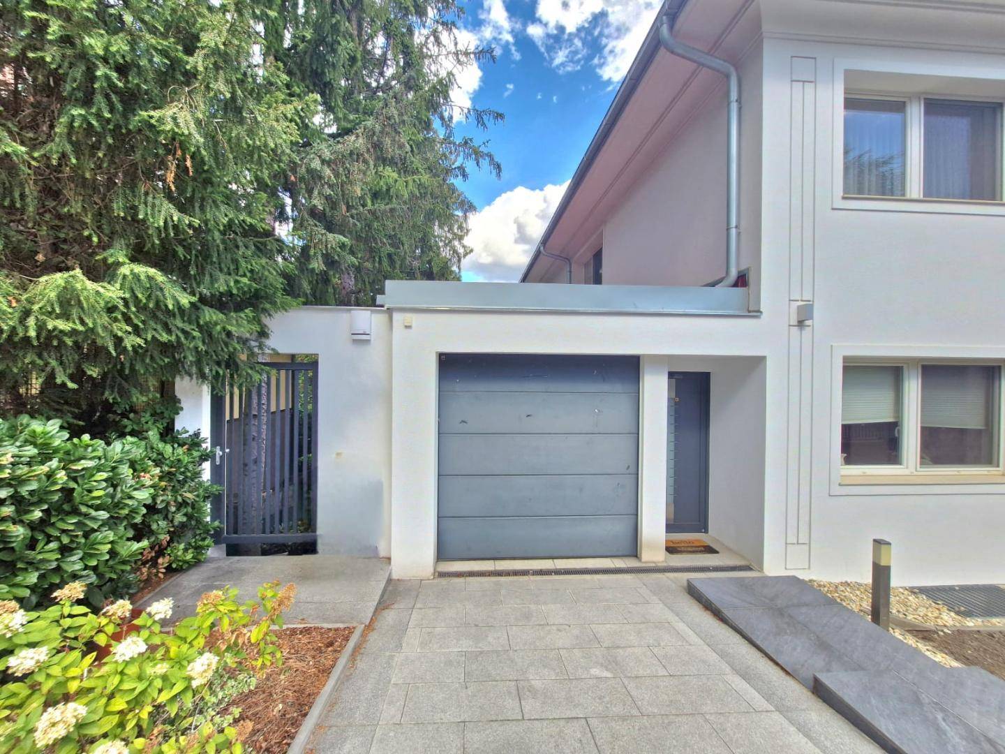 Moderne Hausfassade mit Garage und Zufahrt, umgeben von gepflegter Bepflanzung.