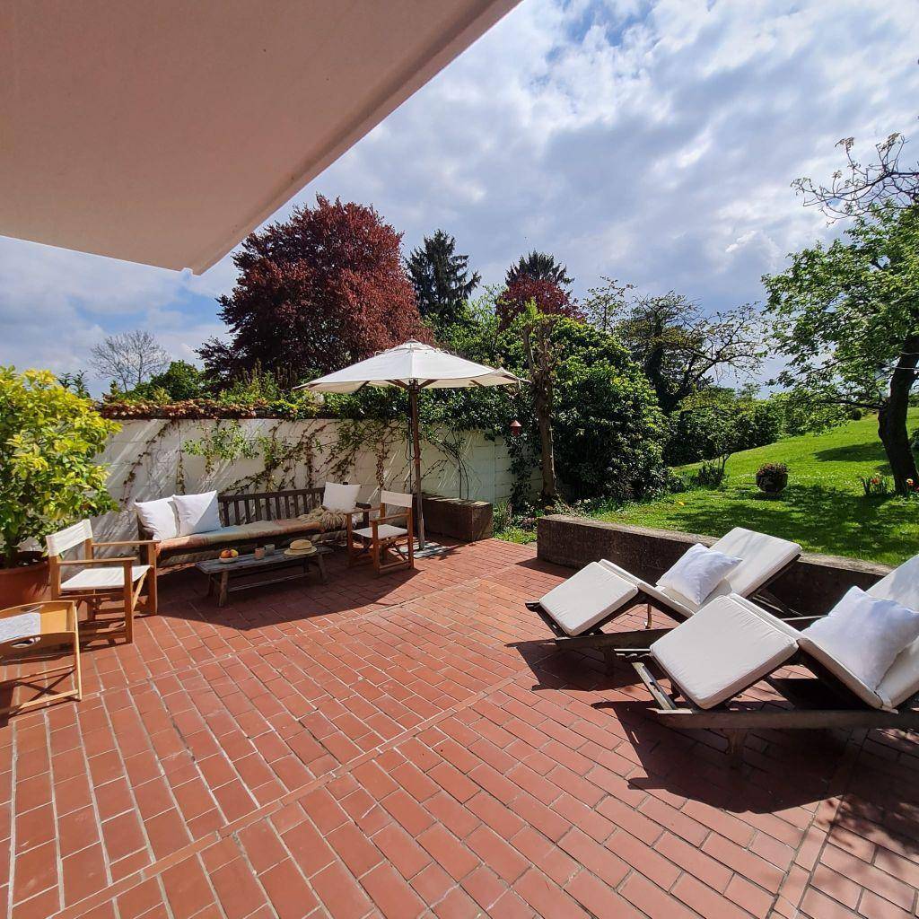 Geräumige Terrasse mit Terrakottafliesen, Sonnenliegen und Essbereich im Grünen.