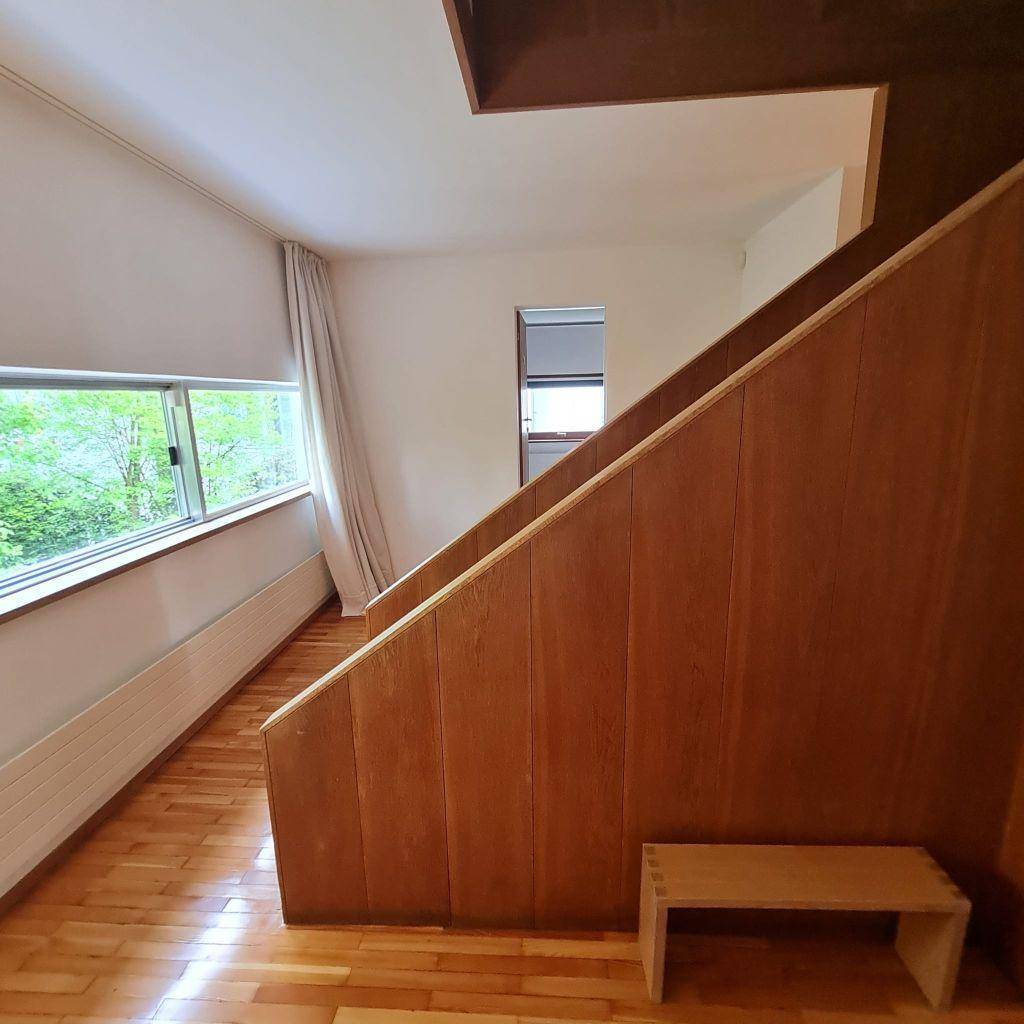 Treppenaufgang mit Holzvertäfelung und großen Fenstern, die viel Tageslicht hereinlassen.