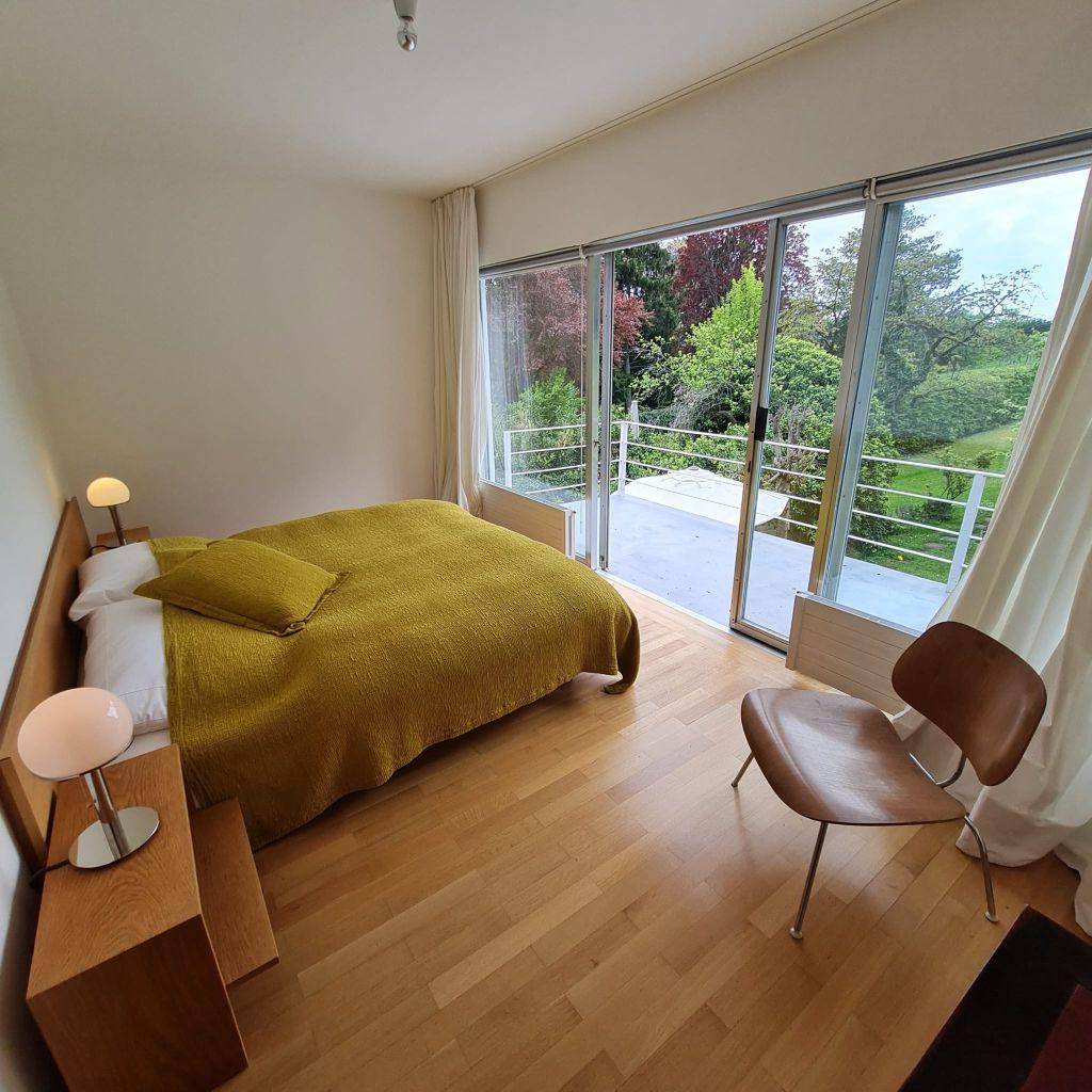 Schlafzimmer mit Holzboden, großen Schiebetüren und direktem Zugang zu einem Balkon mit Gartenblick.