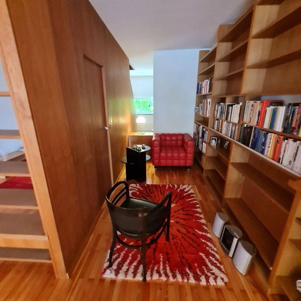 Gemütlicher Bibliotheksbereich mit Holzbücherregalen, rotem Teppich und Lesesessel.