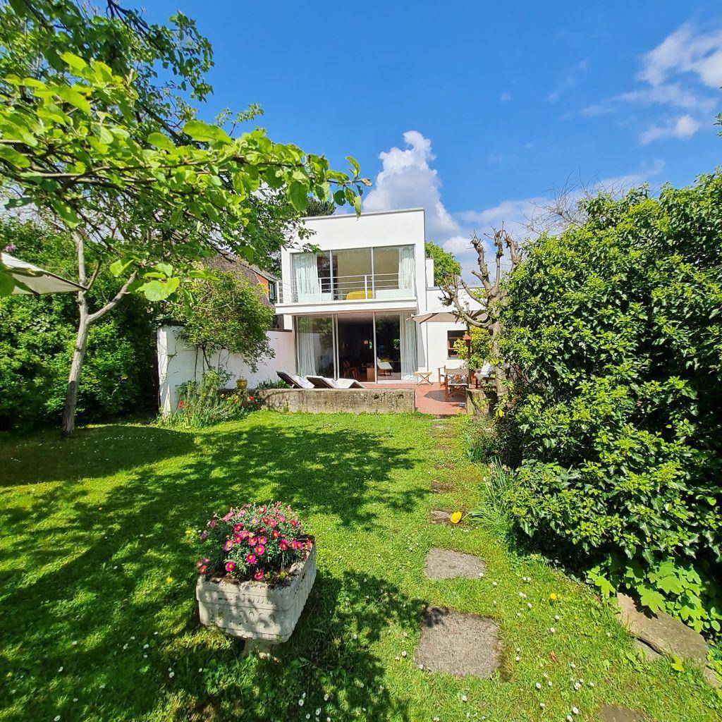 Moderner Hausbau mit großen Fensterfronten und Zugang zu einem weitläufigen, grünen Garten.