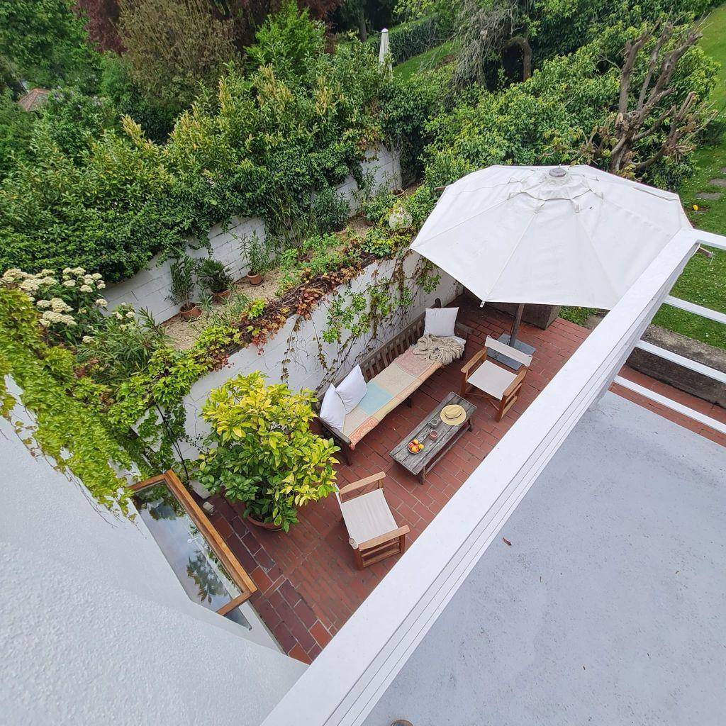 Von oben gesehen: Gemütliche Terrasse mit Sitzgelegenheiten und Sonnenschirm, umgeben von viel Grün.
