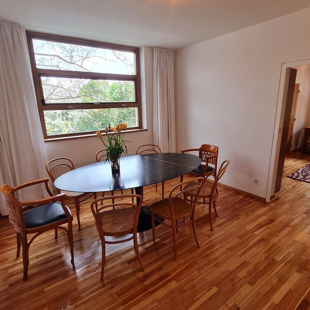 Eleganter Essbereich mit Holzboden, großem ovalen Tisch und Stühlen mit Blick ins Grüne.