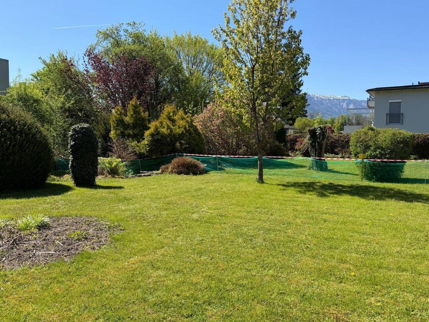 Sonniger Gartenbereich mit Rasen, Bäumen und Blick auf die umliegende Berglandschaft.