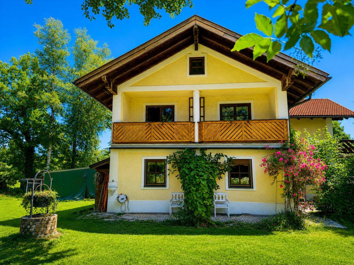 Traditionelles gelbes Haus mit Balkon und einem dekorativen Brunnen im Vorgarten.