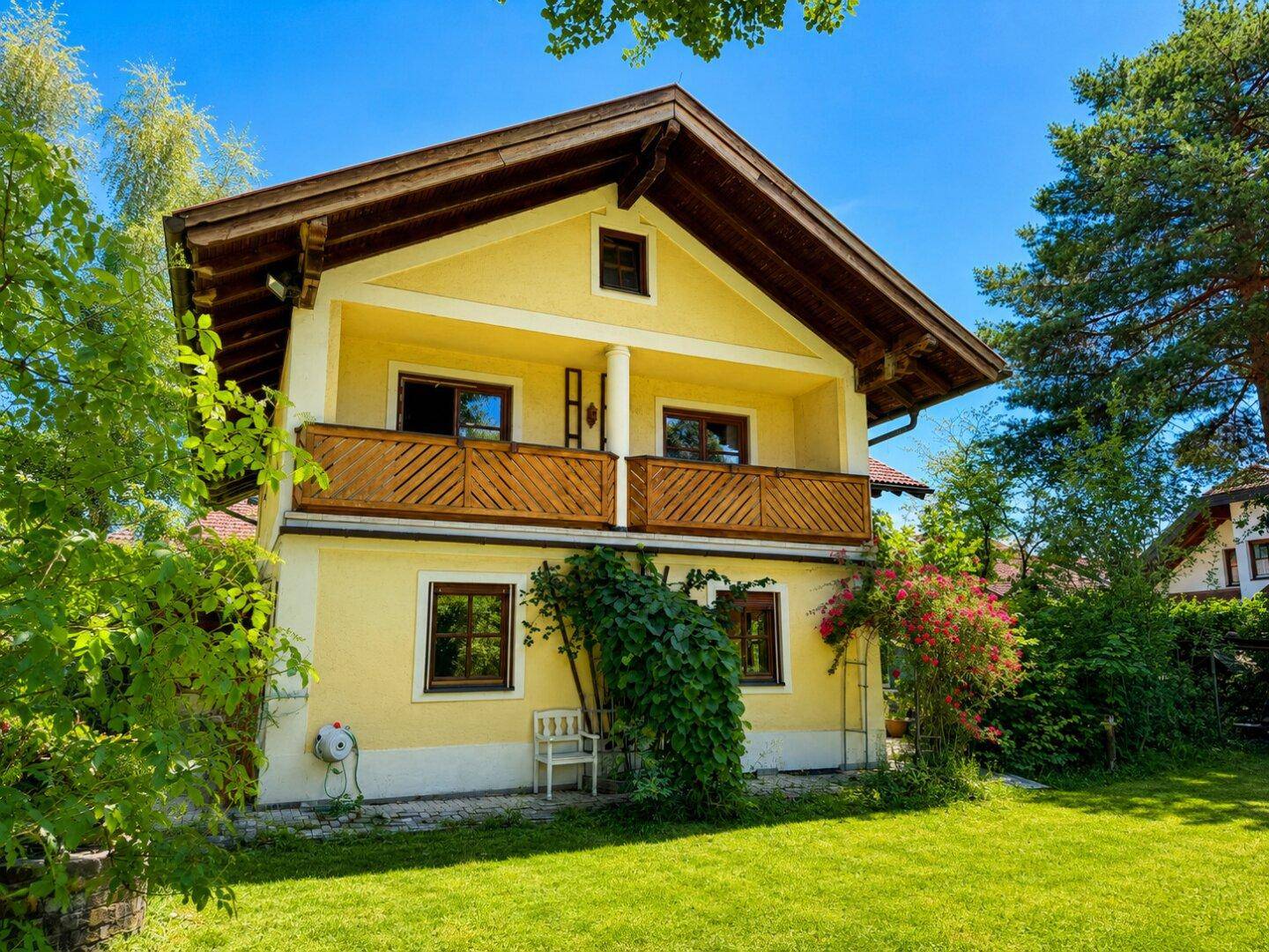 Charmantes gelbes Haus mit Holzbalkon und gepflegtem Rasen unter blauem Himmel.