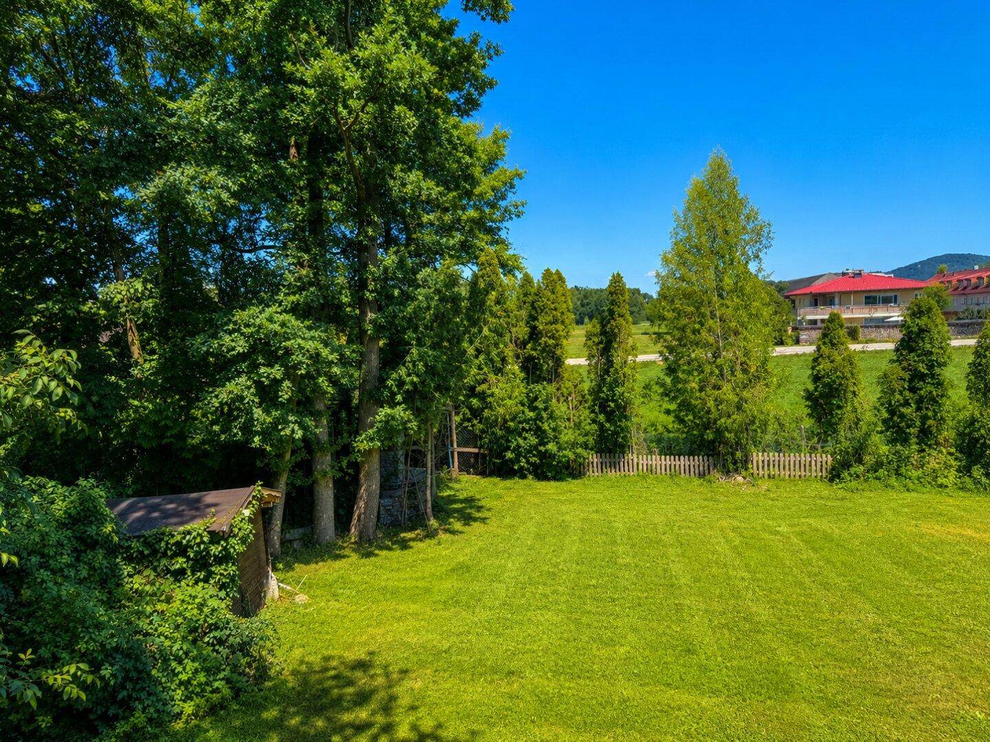 Weitläufiger grüner Garten mit hohen Bäumen und Blick auf die umliegende Landschaft.