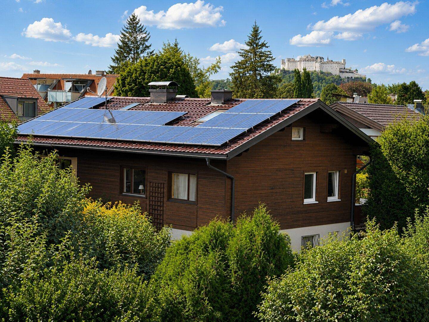 Braunes Haus mit Ziegeldach, Photovoltaikanlage und Blick auf eine historische Festung in der Ferne.