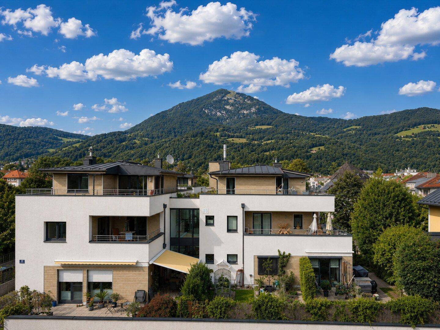 Moderne Wohnanlage mit mehreren Terrassen und Balkonen, eingebettet in eine grüne Berglandschaft.