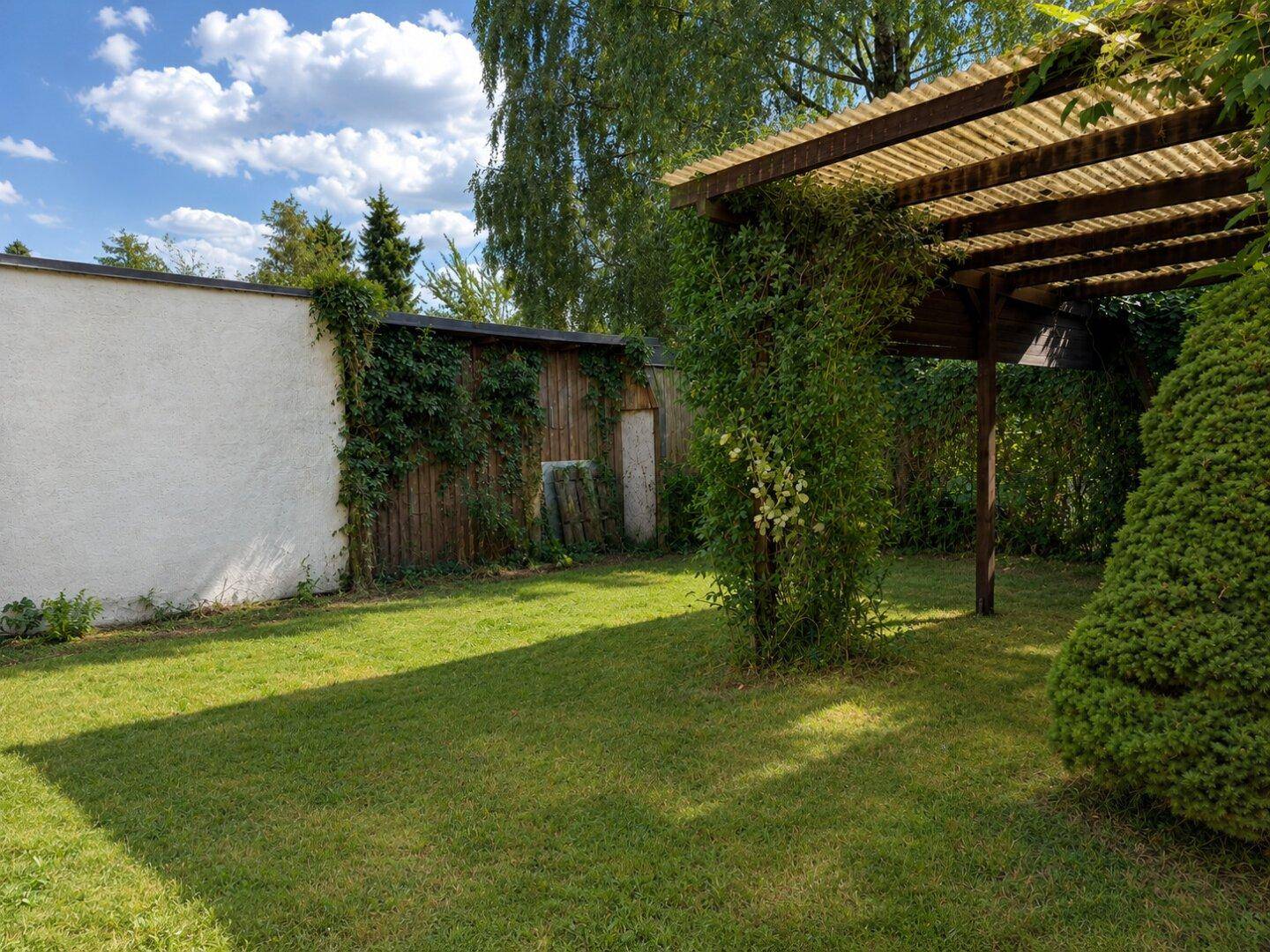 Gepflegter Gartenbereich mit grünem Rasen und einer bewachsenen Holzpergola für entspannte Stunden.