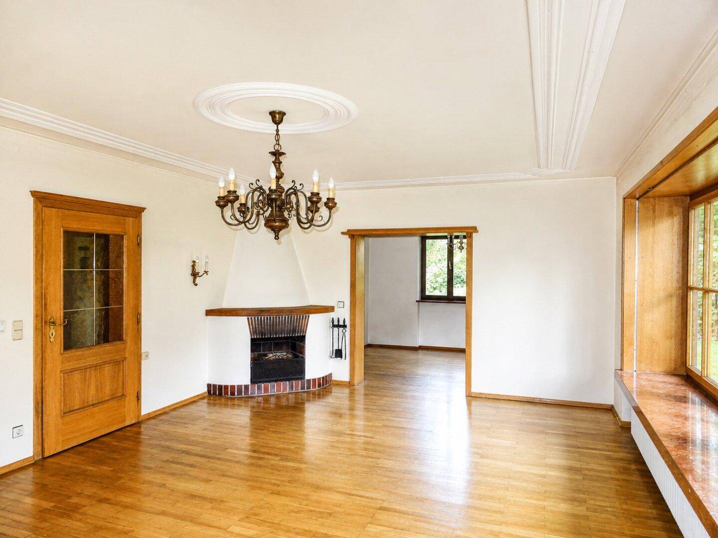 Helles Wohnzimmer mit Parkettboden, klassischem Kamin und Stuckelementen an der Decke.