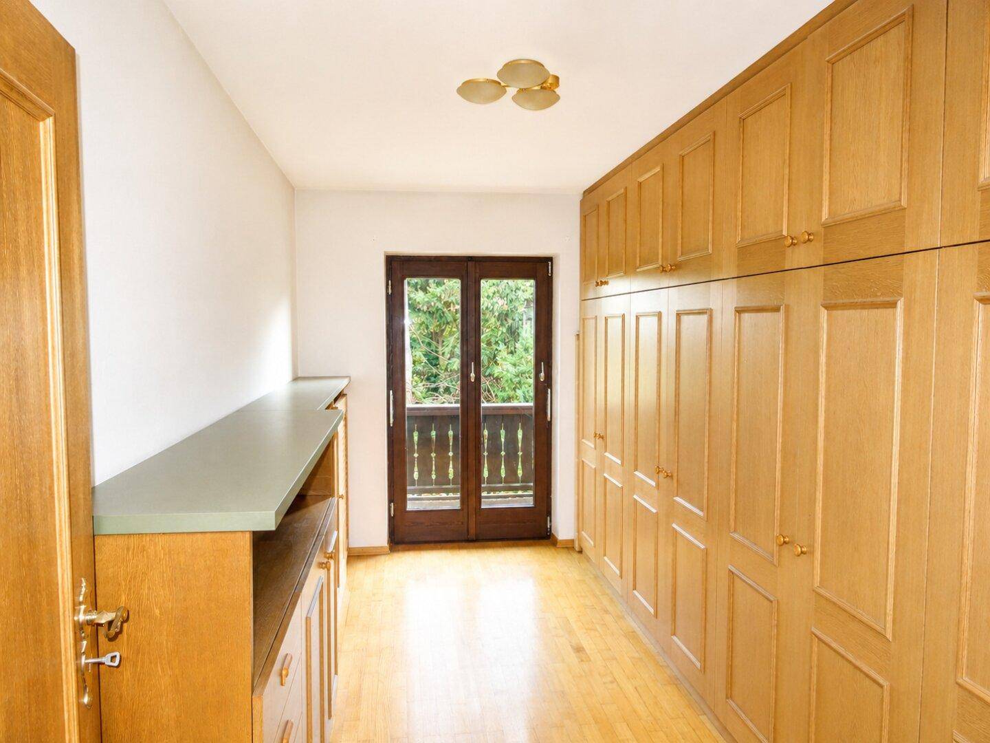Zimmer mit Einbauschränken aus Holz, Parkettboden und Zugang zu einem Balkon.