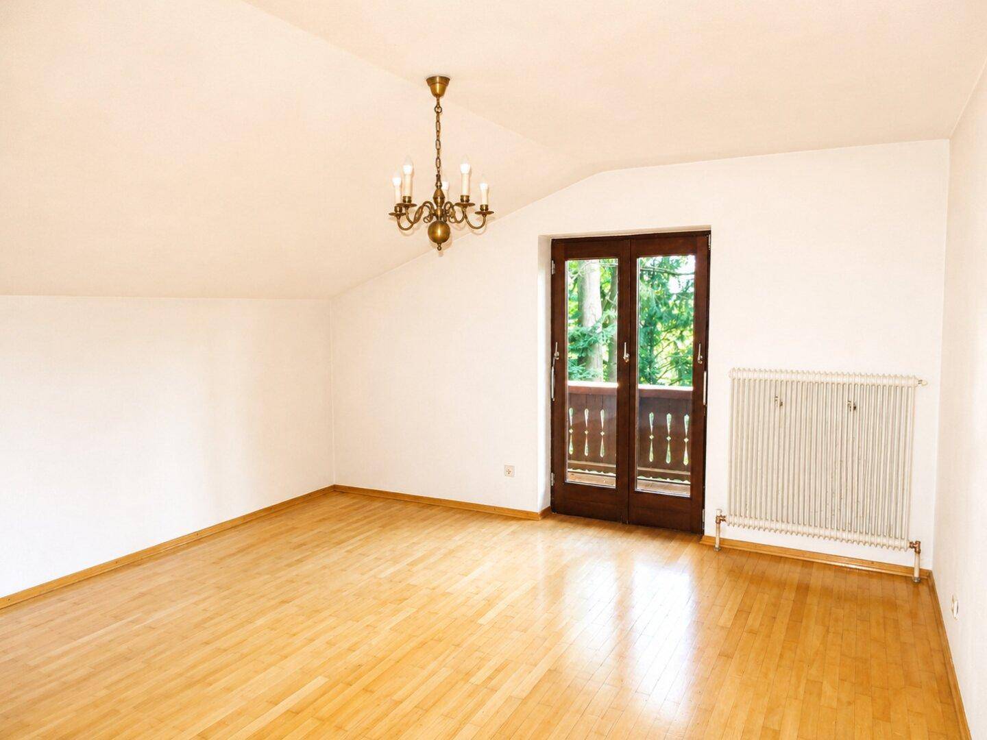 Geräumiges Zimmer im Dachgeschoss mit Parkettboden, Heizkörper und Balkonzugang.